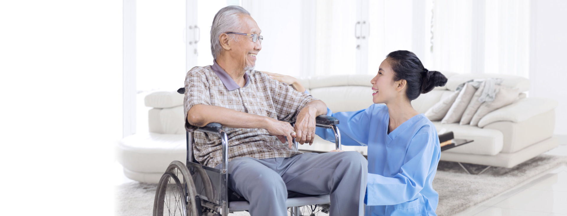 Senior man in a wheelchair and nurse facing each other while smiling